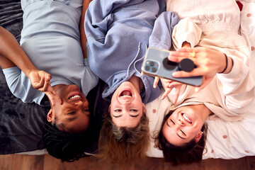 Overhead Shot Of Multi-Cultural Teenage Girl Friends Posing For Selfie On Mobile Phone At Home