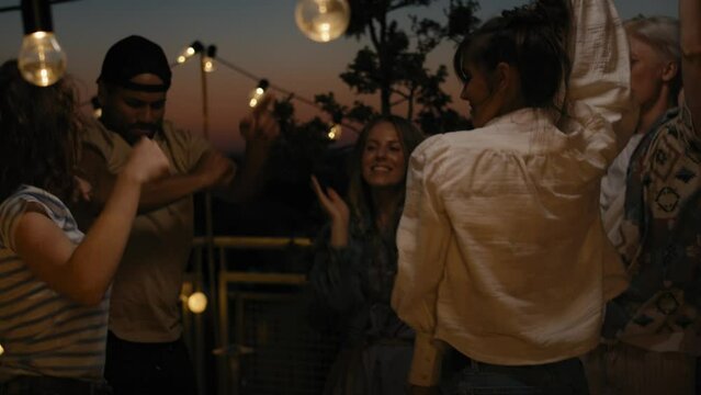 Group of friends dancing at the party in top of the roof at night. Shot with RED helium camera in 8K.  