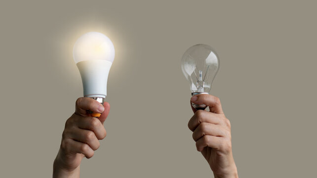 Power saving concept. Hands holding new Light Emitting Diode ( LED ) light bulb with light on and blur spiral compact-fluorescent (CFL) bulbs behind for copyspace.
