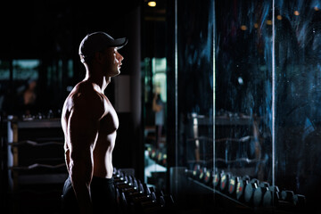 Fototapeta na wymiar muscular man working out with dumbbells in gym dark tone,
