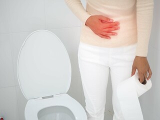 Woman holding a paper roll and suffering from diarrhea at toilet. health care concept. Closeup photo, blurred.