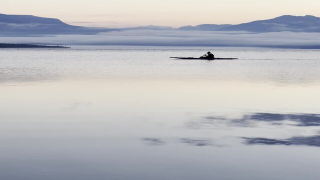Kayaker glides across the lake during early morning sunrise