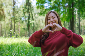 Portrait image of a beautiful asian woman making heart hand sign in the park
