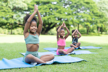 African American little girls sitting with closed eyes practicing meditate yoga on roll mat in the park.