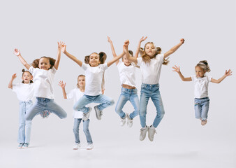 Portrait of happy, active little girls, sportive kids in casual clothes dancing isolated on white...