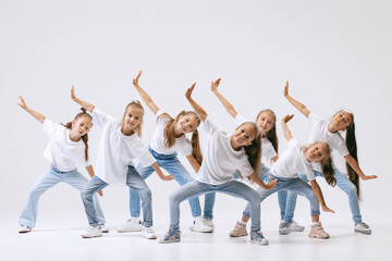 Dance group of happy, active little girls in jeans and t-shirts dancing isolated on white studio background. Concept of music, fashion, art, childhood, hobby