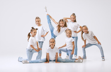 Portrait of happy, active little girls, sportive kids in casual clothes dancing isolated on white...