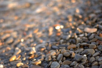 A transparent sea wave rolls over a rocky beach, the concept of rest and travel, calmness and reflection on a warm summer day, defocusing, blurred background, selective focus, bokeh.