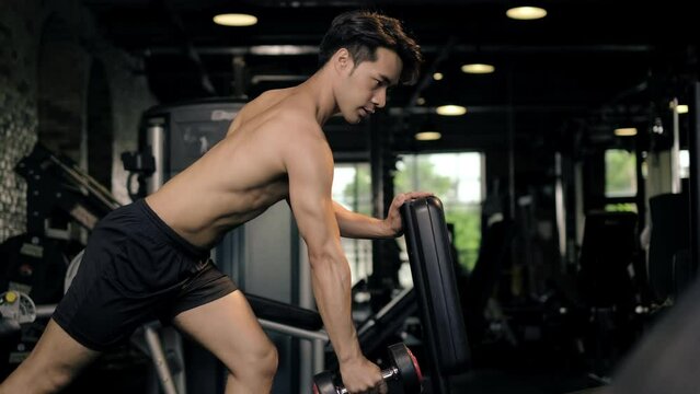 4K footage young Asian man workout lifting up bumbbell in the indoor gym. Physical and muscle weight training for body building workout. Weight exercise at fitness gym.