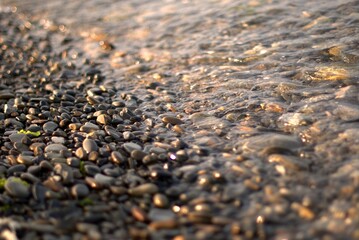 A transparent sea wave rolls over a rocky beach, the concept of rest and travel, calmness and reflection on a warm summer day, defocusing, blurred background, selective focus, bokeh.