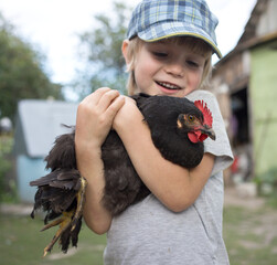 Caucasian boy holding a chicken in his arms. Happy child spends summer on the farm. Treating poultry, interesting childhood. Selective focus