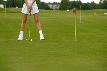 Woman in white short skirt practicing golf on the green