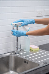 Close up of female hand in protective gloves blue wiping dust using spray and cloth while cleaning her kitchen.Cleaning and housekeeping concept