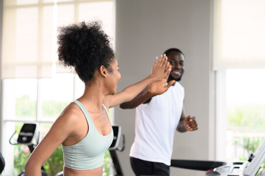 Black African American couple clapping hands together while running on the treadmill at fitness club. Healthy lifestyle, training in gym. Fitness partners give a high five. healthy concept.