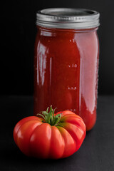 Tomatoes and a jar of home canned tomato sauce on a black background