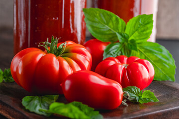 Fresh ripe, whole tomatoes, basil and home canned tomato sauce on a wooden cutting board