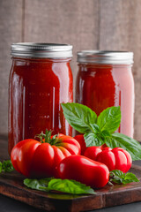 Fresh ripe, whole tomatoes, basil and home canned tomato sauce on a wooden cutting board