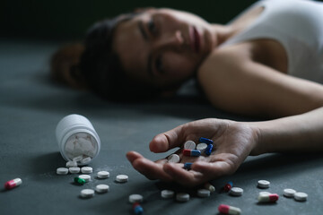 Young woman overdosed with pill bottle and pills on the floor.Selective focus on hand.
