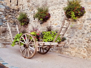 Fototapeta na wymiar Cart with flowers background. Prats-de-Mollo-la-Preste village. Eastern Pyrenees and the region of Occitanie, in the Vallespir region. Villages of the South of France.