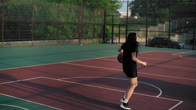 Female basketball player on professional court running with ball and thowing ball to the hoop. A teenage girl trains to fill a ball on a basketball court.