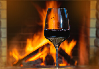 Glass of red wine before a cozy burning fireplace in country house.