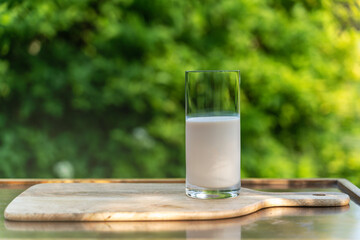 A glass of milk on a wooden desk against the background of nature in a garden.
