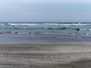 The shore of the Celtic Sea at low tide. Wet sandy beach on a cool day. Minimalistic seascape. Cloudy cool weather.