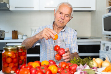 Fototapeta premium old gray haired man makes harvests for the winter pickles tomatoes