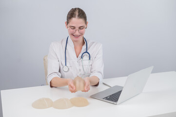 Woman plastic surgeon demonstrating breast implants at her desk. 