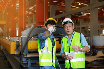 Two Asian male engineers use a tablet to discuss production plans and inspect production machines.