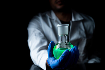 A woman scientist experimenting with a green fluorescent solution in a glass round bottom flask in dark chemistry laboratory