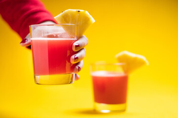 Woman holding Pineapple juice in glass closeup near sliced fruit with spash and dripping liqid for summer vibes.