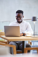 A freelancer is typing on the keyboard while smiling at the laptop in the cafeteria.