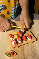 A little boy is playing plasticine. He made sushi and rolls
