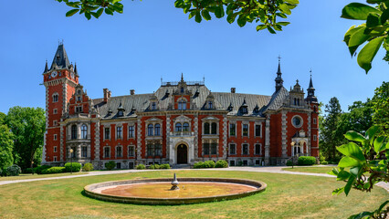 The Palace in Plawniowice, the palace and park complex from the 1980s. A magnificent building made of red brick with numerous decorations, the view on a sunny summer day.