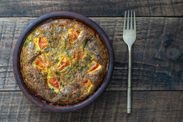 Ceramic bowl with vegetable frittata, simple vegetarian food, top view. Frittata with egg, tomato, pepper, onion, dill, parsley and cheese. Italian egg omelette