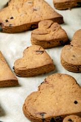 Heart shaped biscuits with chocolate drops on a baking tray.