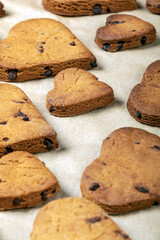 Heart shaped biscuits with chocolate drops on a baking tray.