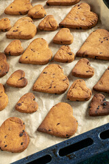 Heart shaped biscuits with chocolate drops on a baking tray.