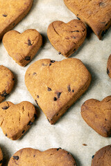 Heart shaped biscuits with chocolate drops on a baking tray.