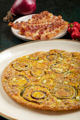 Homemade onion omelette in a white dish, crispy bacon slices and red chili peppers on the background.