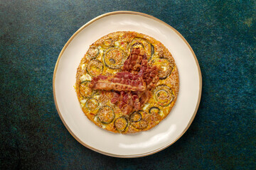 An onion omelette with red chili peppers, sesame seeds and some crispy bacon slices placed on top.