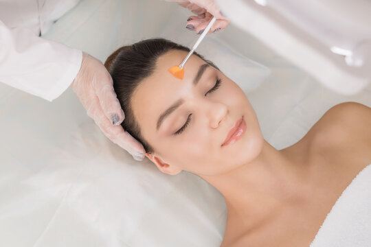 Cosmetic procedure. Chemical peeling. Doctor's hand with a brush touching the face of a young beautiful woman. Facial skin care. Place for text.