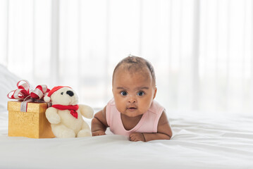 African baby newborn is 3-month-old lying on the white bed next to a gift box and teddy bear, to the best gift for family is a child and newborn concept.