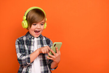 Photo of young excited boy look mobile listen music headphones button isolated over orange color background