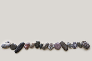 Top view close up dark pebbles sea stones on sand color background. Row from natural round smooth stone black. Minimal style flat lay, summer concept, empty space