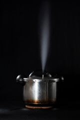 Close-up of a pressure cooker releasing steam through the lid, against a black background