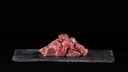 Raw beef, cubed and sprinkled with spices, on a slate and black background