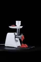 Meat grinder chopping red meat, on black background