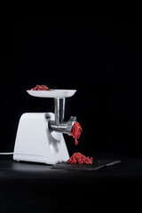 Meat grinder chopping red meat, on black background
